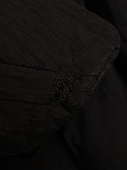 Close-up detail of a black quilted fabric item, showing stitched paneling and a small textured accent.