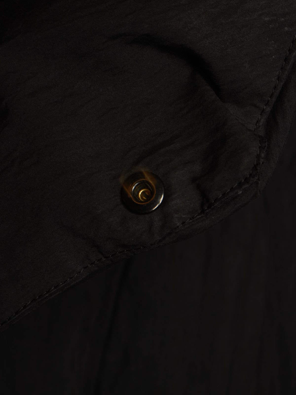 Close-up of a black garment with a small metallic snap button detail.