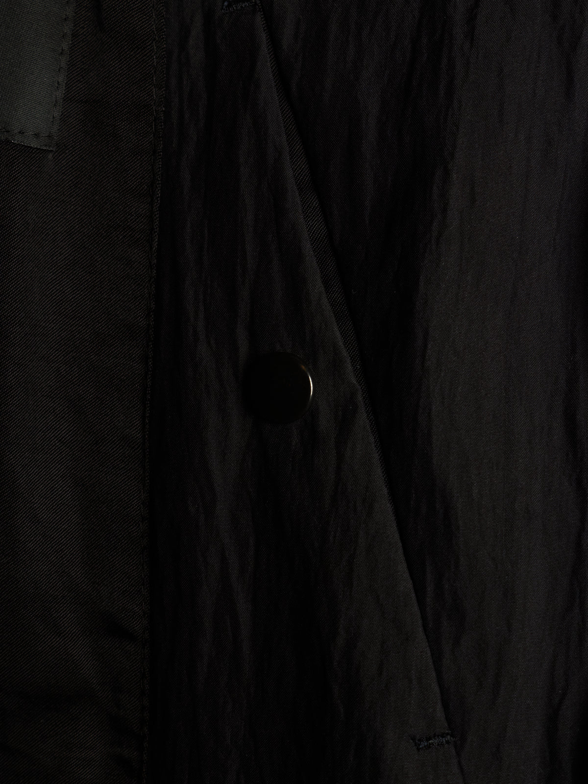 Close-up of a black textured fabric garment with a dark button and subtle tonal stitching.