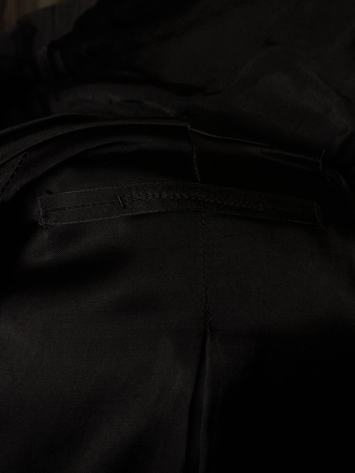 Close-up detail of black fabric with a horizontal stitched welt pocket and visible seam lines.