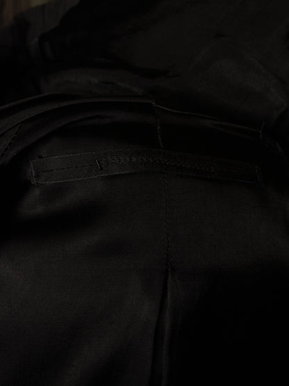 Close-up detail of black fabric with a horizontal stitched welt pocket and visible seam lines.