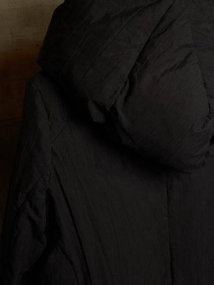 Close-up of a black quilted puffer jacket with a hood, showing the padded texture and stitching details.