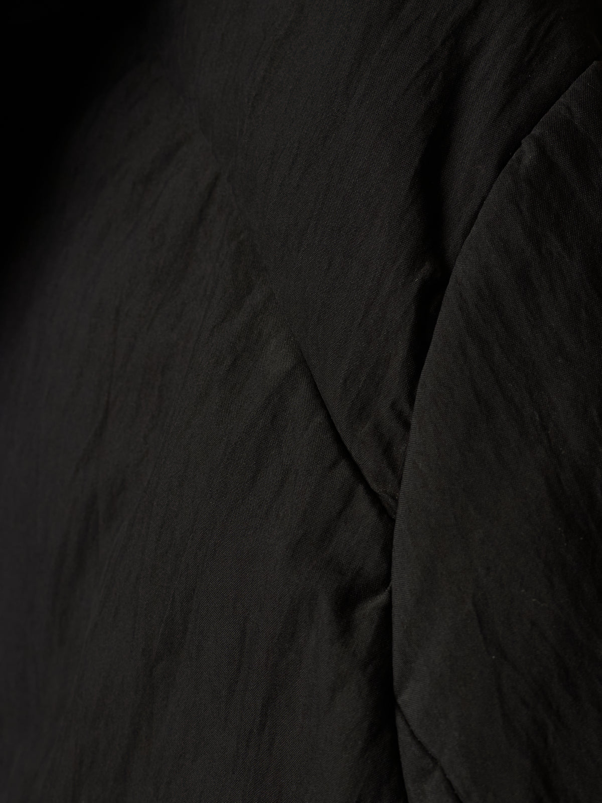 Close-up of a black crinkled fabric texture with soft folds and shadows.