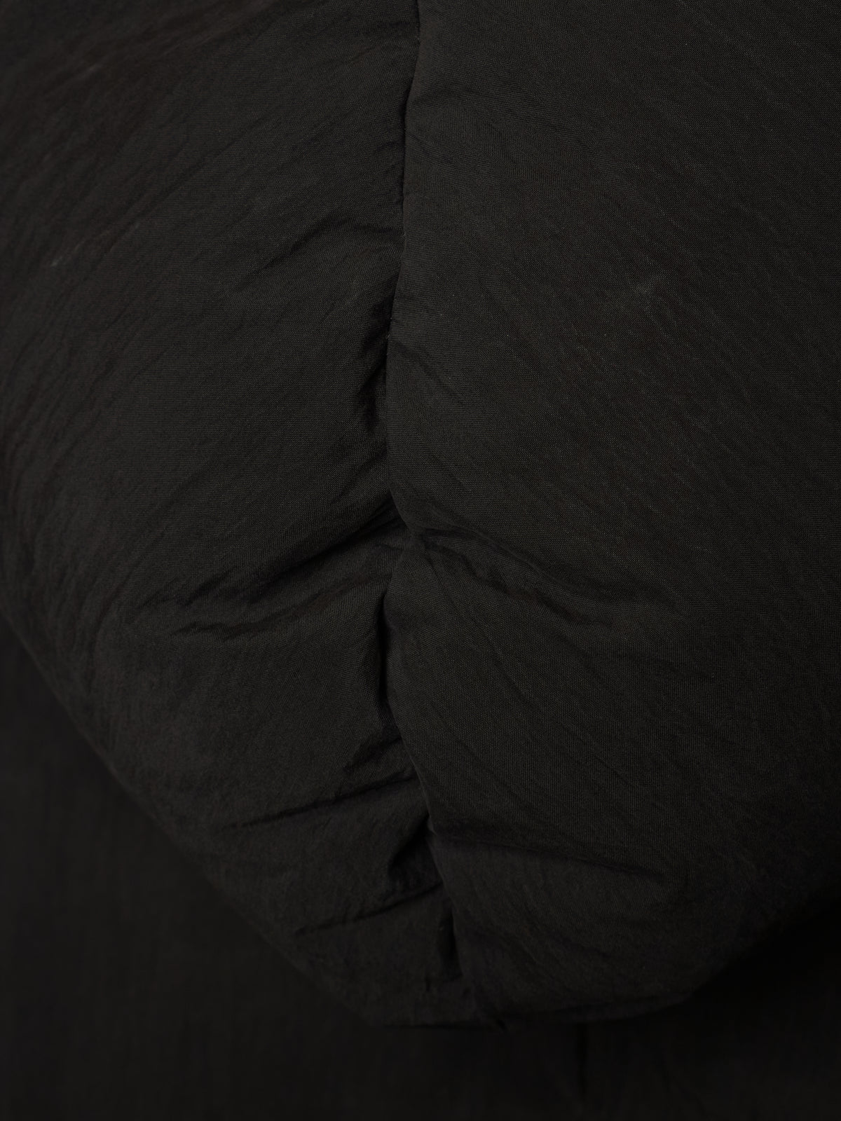 Close-up of a black quilted fabric surface with visible stitched padding and a crinkled texture.