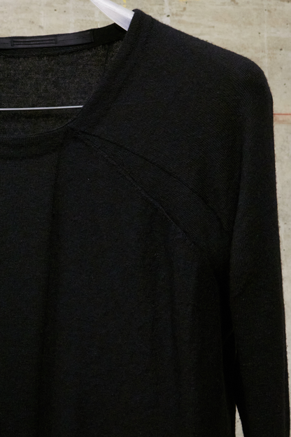 Black long-sleeve shirt on a hanger against a beige wall.