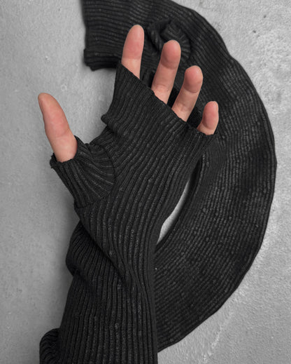 A hand wearing DRIEW’s Julius_7 AW24-25 “rift;” Curved Wax Coated black, ribbed, fingerless glove with a thumb hole rests on a textured gray surface, matching the fabric coiled beside it. One size; extends up the arm.