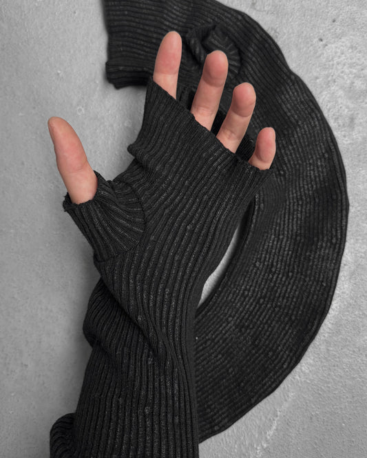 A hand wearing DRIEW’s Julius_7 AW24-25 “rift;” Curved Wax Coated black, ribbed, fingerless glove with a thumb hole rests on a textured gray surface, matching the fabric coiled beside it. One size; extends up the arm.