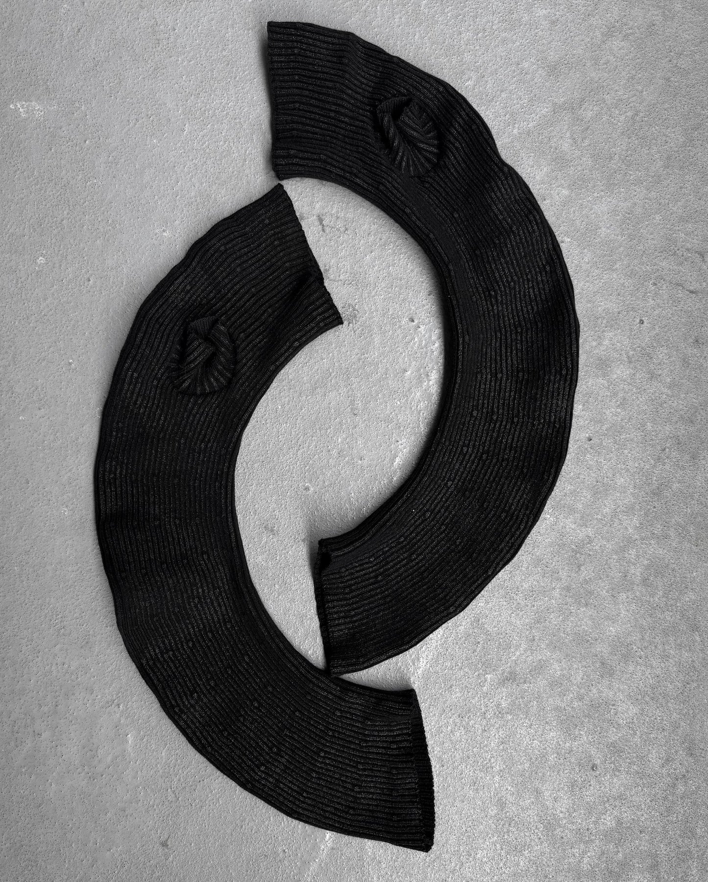 Two curved, ribbed black Julius_7 AW24-25 “rift;” Curved Wax Coated Gloves by DRIEW, with flawless circular textured details, are arranged on a light gray surface in a C-shape. One size fits all for versatile styling.