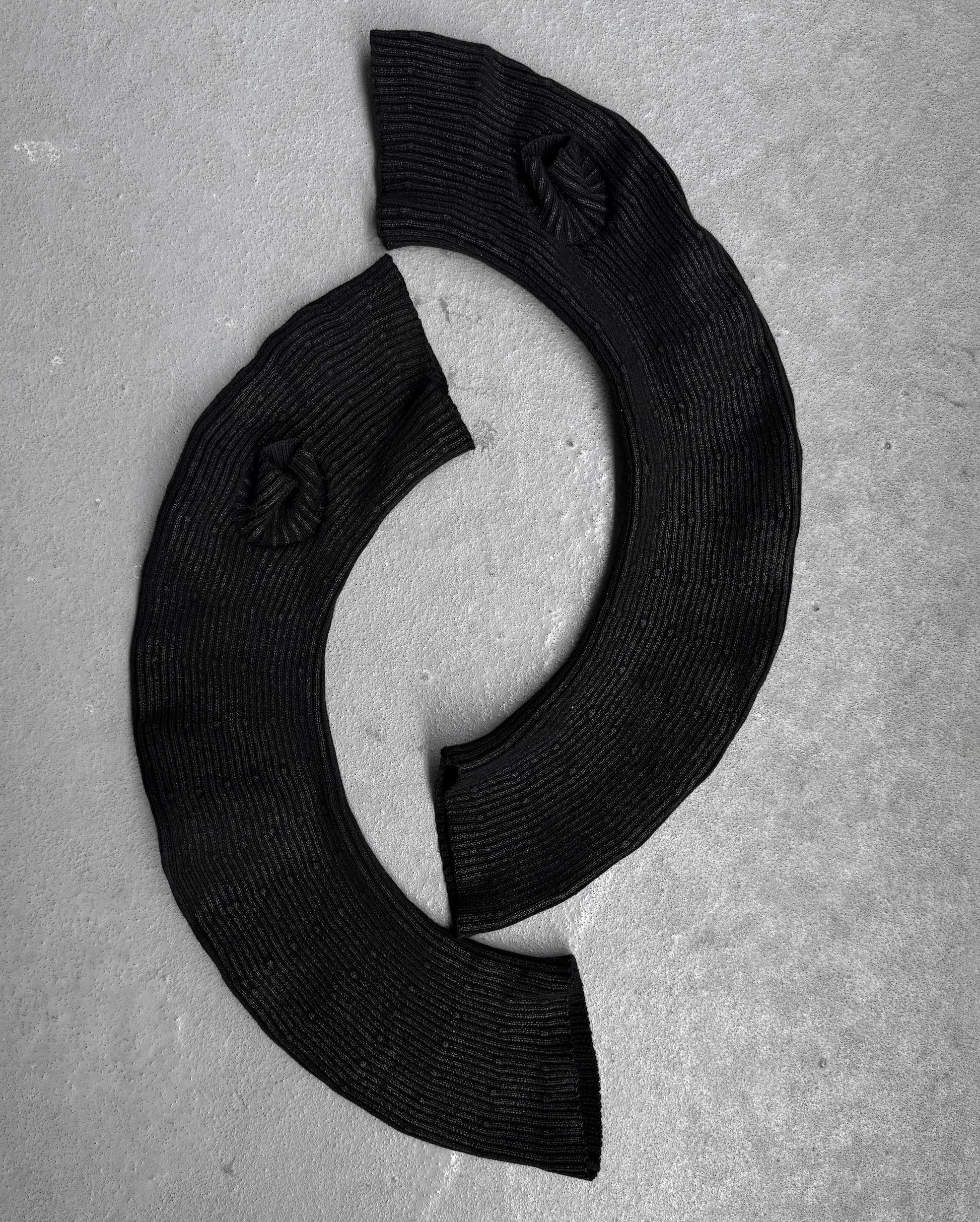 Two curved, ribbed black Julius_7 AW24-25 “rift;” Curved Wax Coated Gloves by DRIEW, with flawless circular textured details, are arranged on a light gray surface in a C-shape. One size fits all for versatile styling.