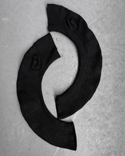 Two curved, ribbed black Julius_7 AW24-25 “rift;” Curved Wax Coated Gloves by DRIEW, with flawless circular textured details, are arranged on a light gray surface in a C-shape. One size fits all for versatile styling.