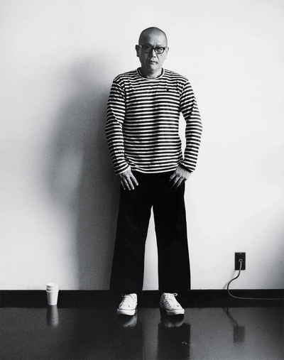 Portrait of Junya Watanabe, Japanese avant-garde fashion designer, standing against a neutral wall in his Tokyo studio