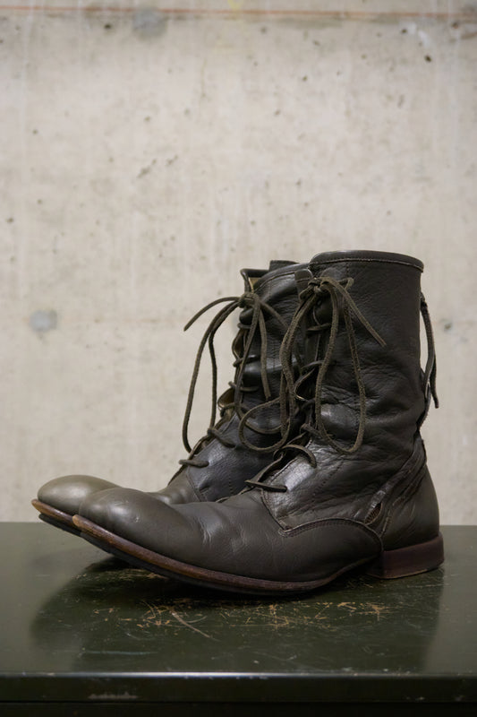 Pair of black leather lace-up boots on a dark surface with a light gray textured background
