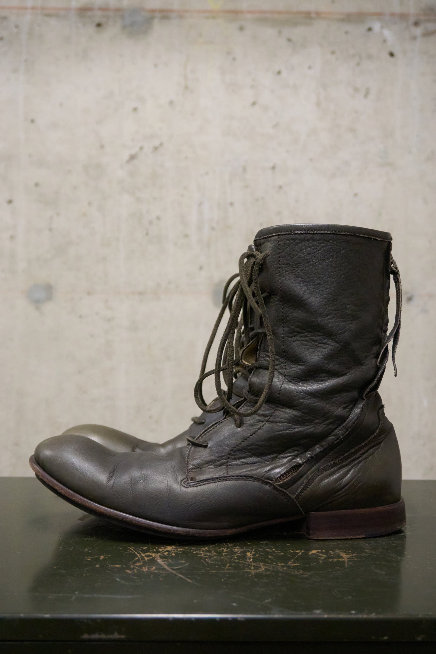 Dark brown leather boot on a textured surface with a neutral background