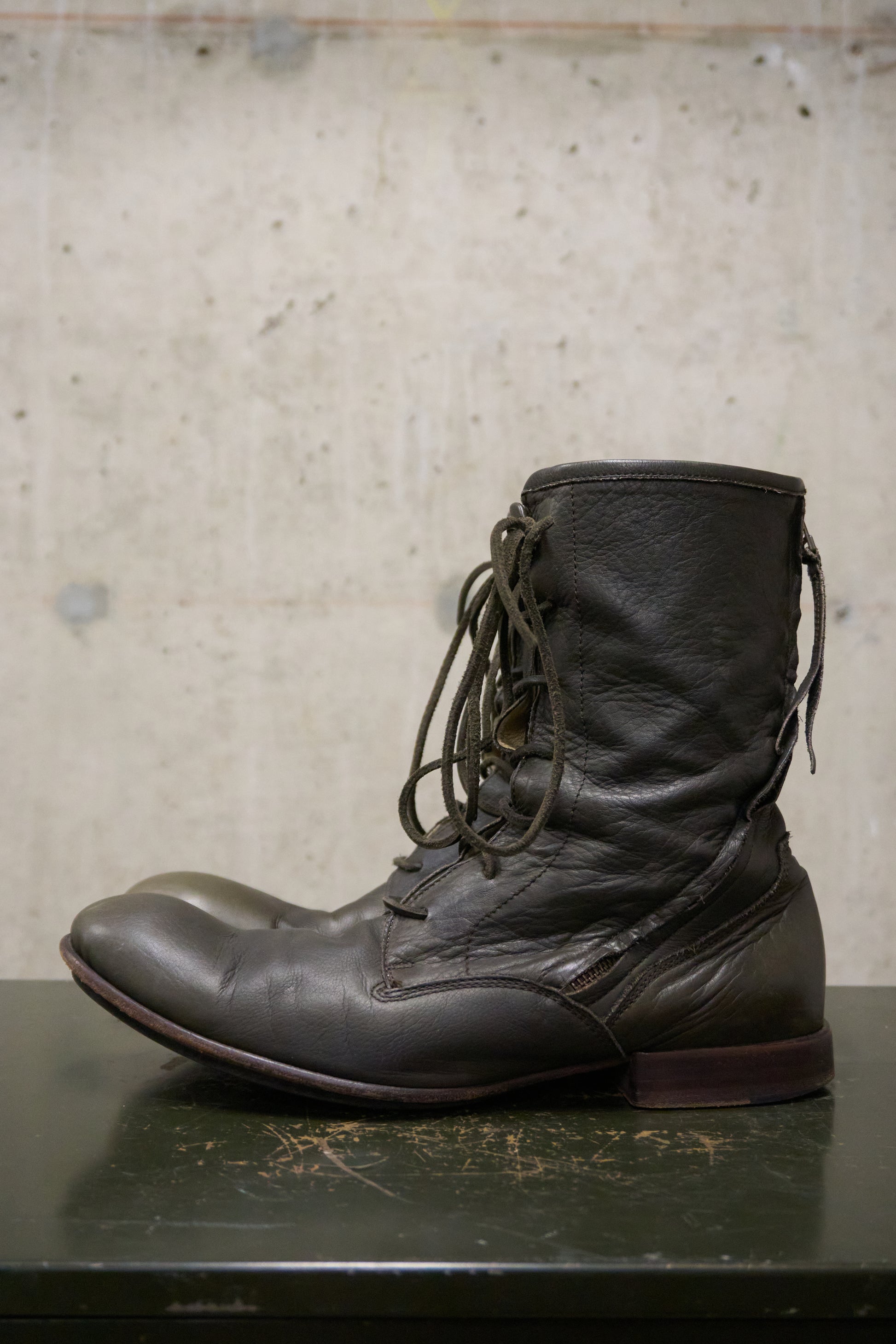Dark brown leather boot on a textured surface with a neutral background