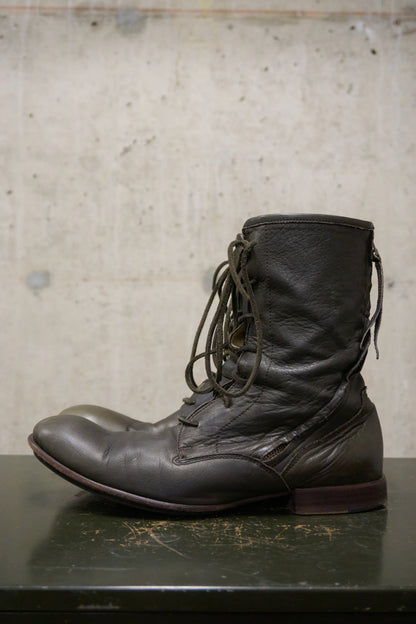 Dark brown leather boot on a textured surface with a neutral background