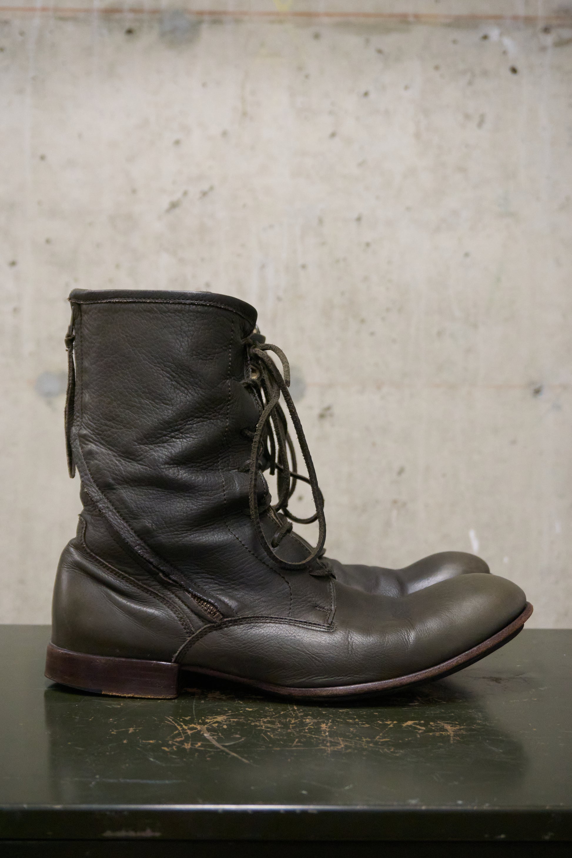 Brown leather boot on a textured surface with a neutral background