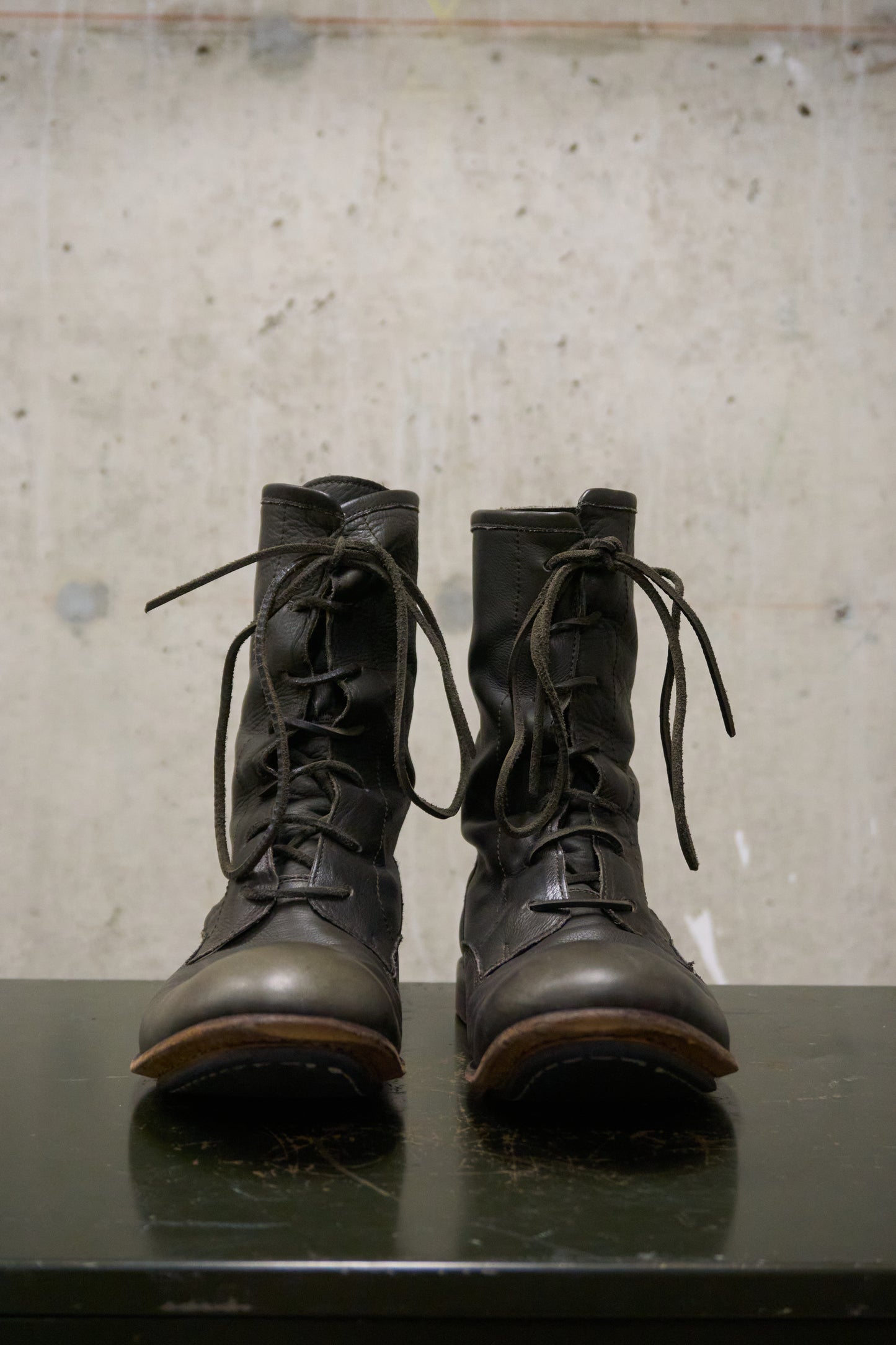 Pair of black leather boots on a reflective surface with a textured gray background