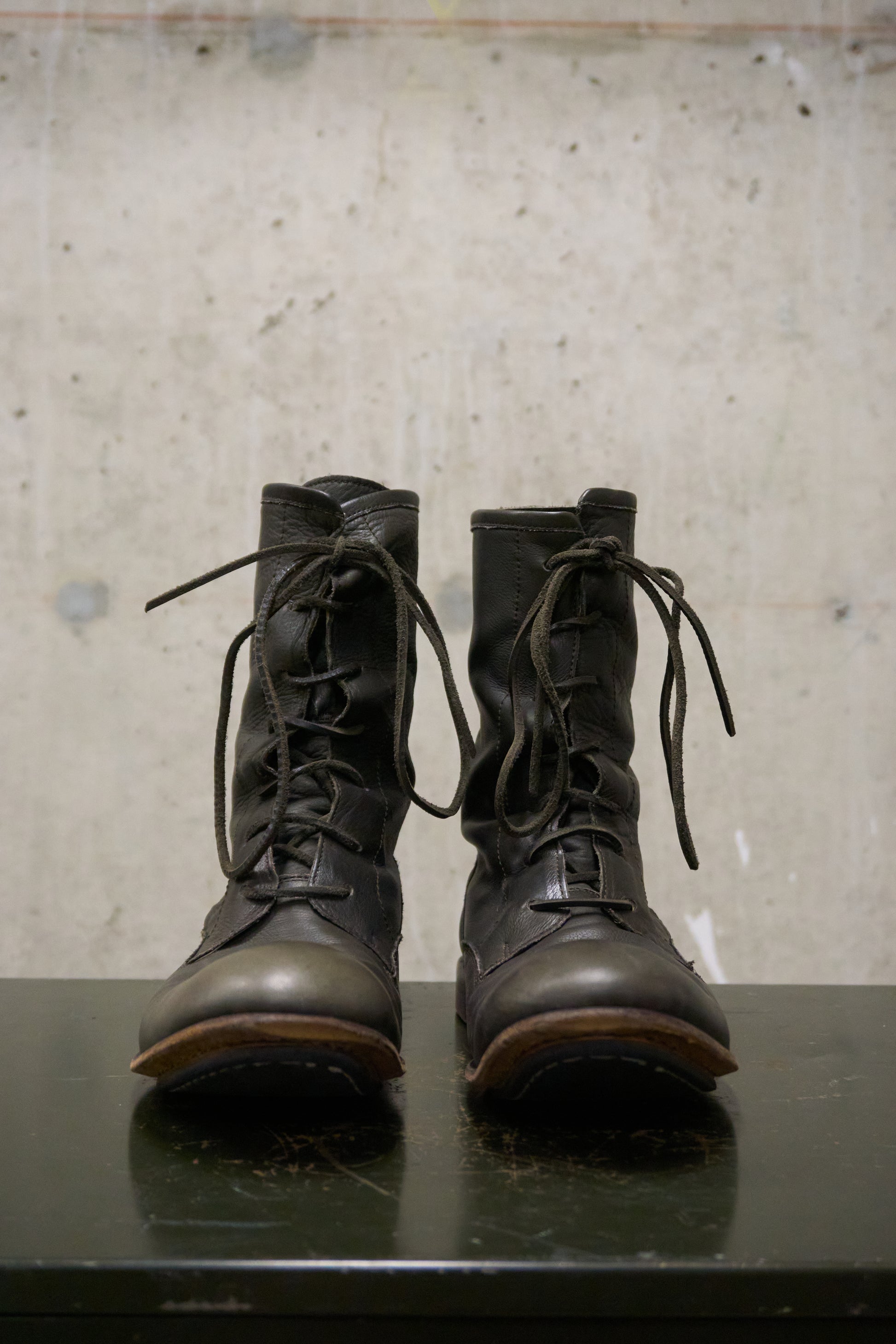 Pair of black leather boots on a reflective surface with a textured gray background
