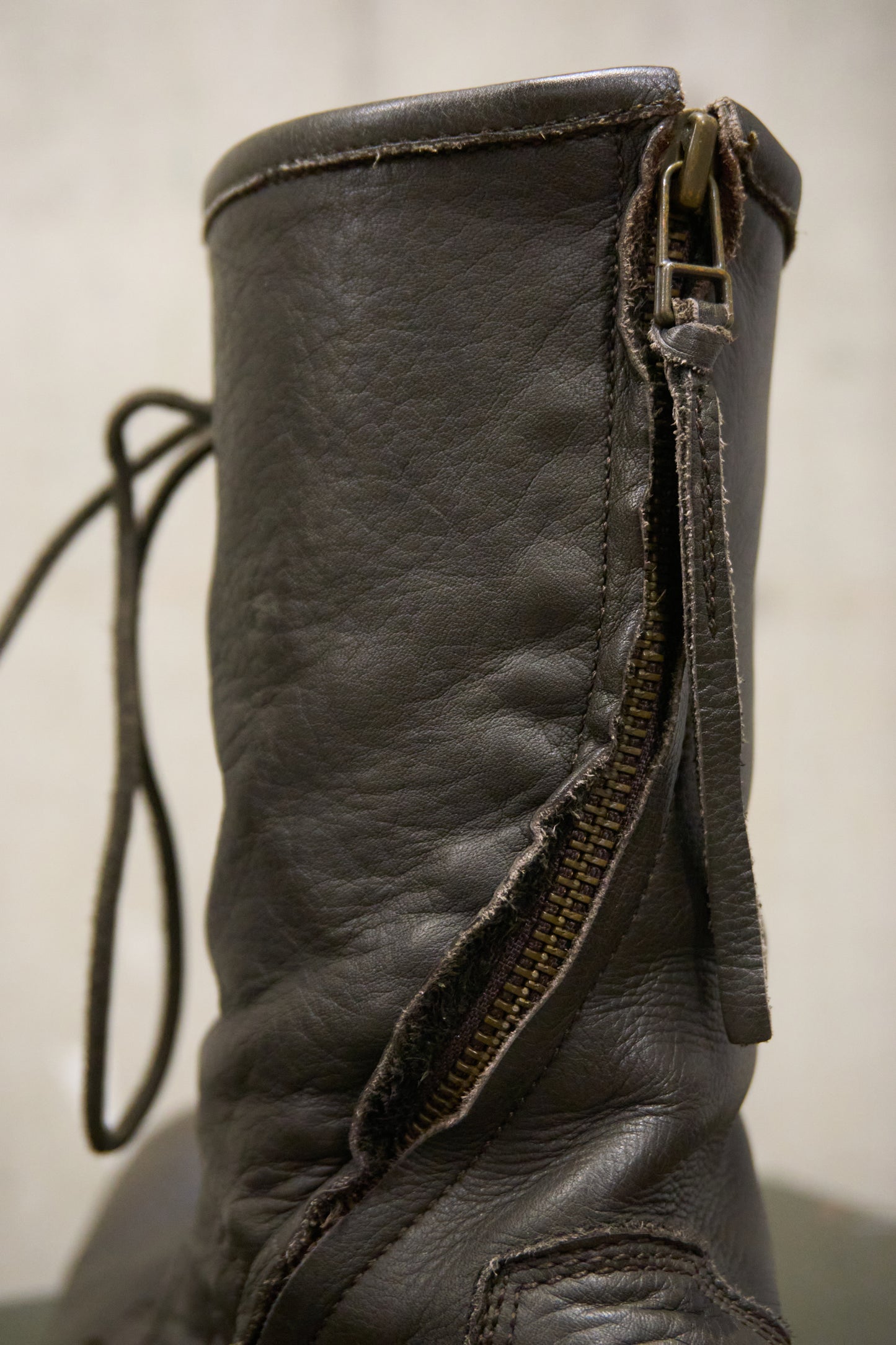Close-up of a worn leather boot with a visible zipper on a plain background