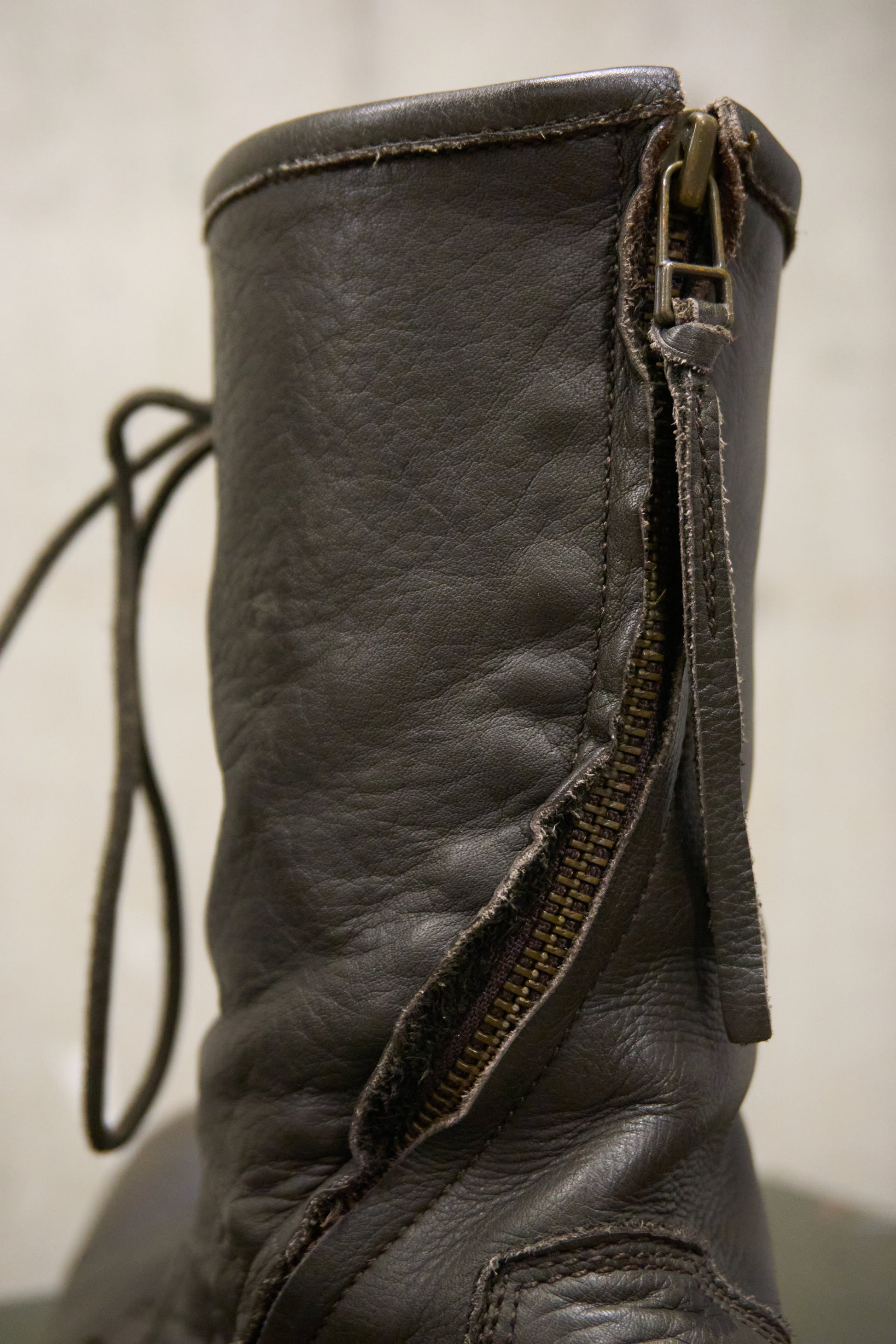 Close-up of a worn leather boot with a visible zipper on a plain background