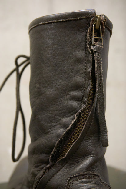 Close-up of a worn leather boot with a visible zipper on a plain background
