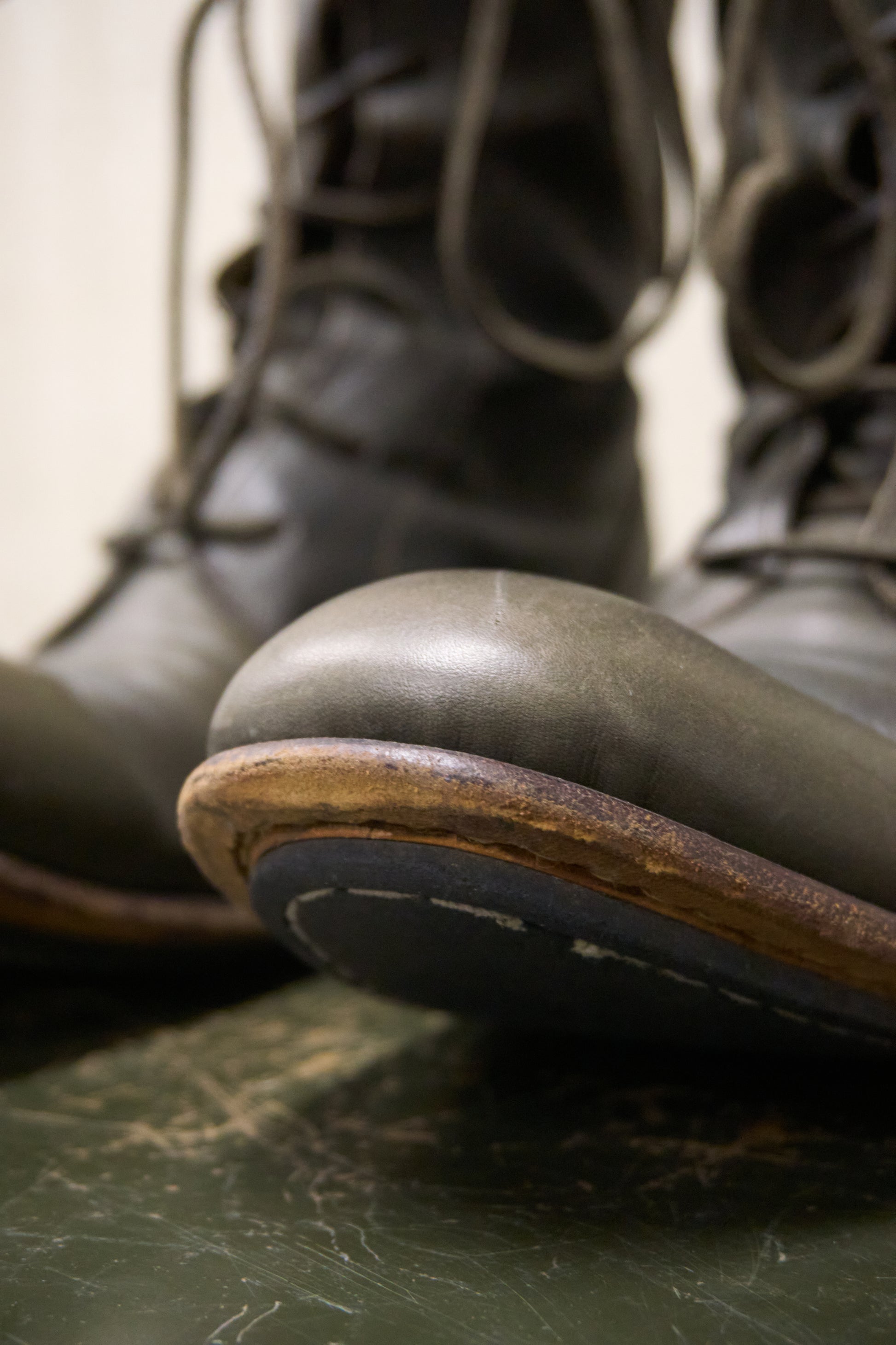 Close-up of green leather boots with brown soles on a marble surface.