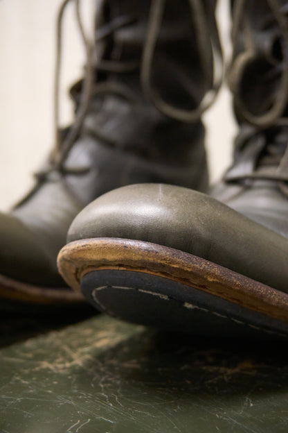 Close-up of green leather boots with brown soles on a marble surface.
