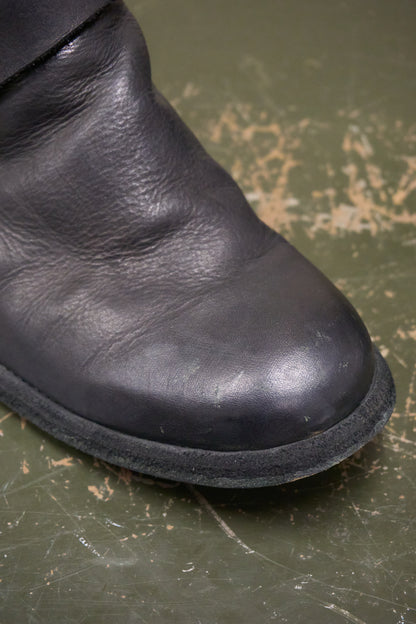 Close-up of a black leather boot on a green surface with visible wear.