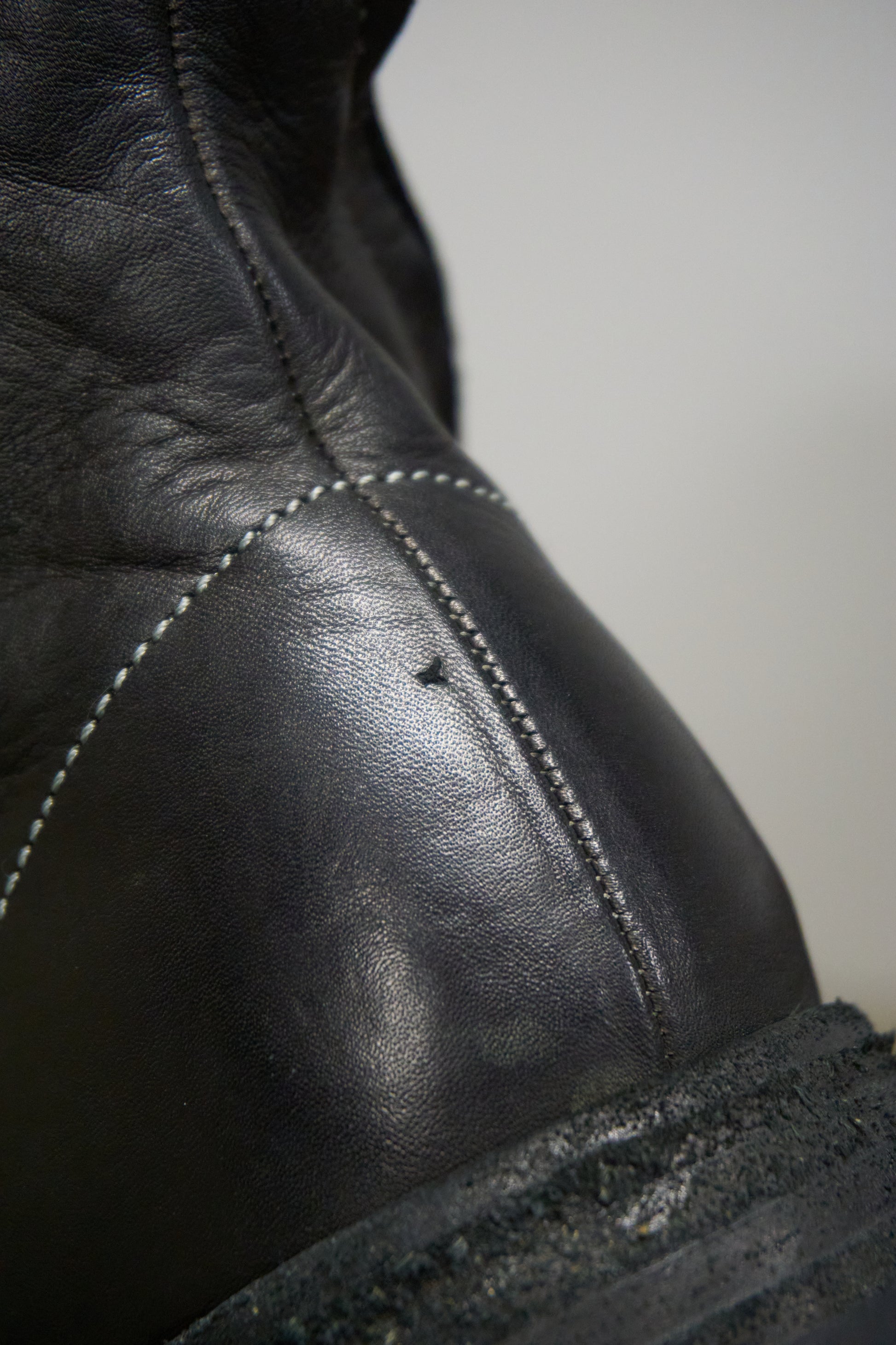 Close-up of a black leather boot with visible stitching on a neutral background