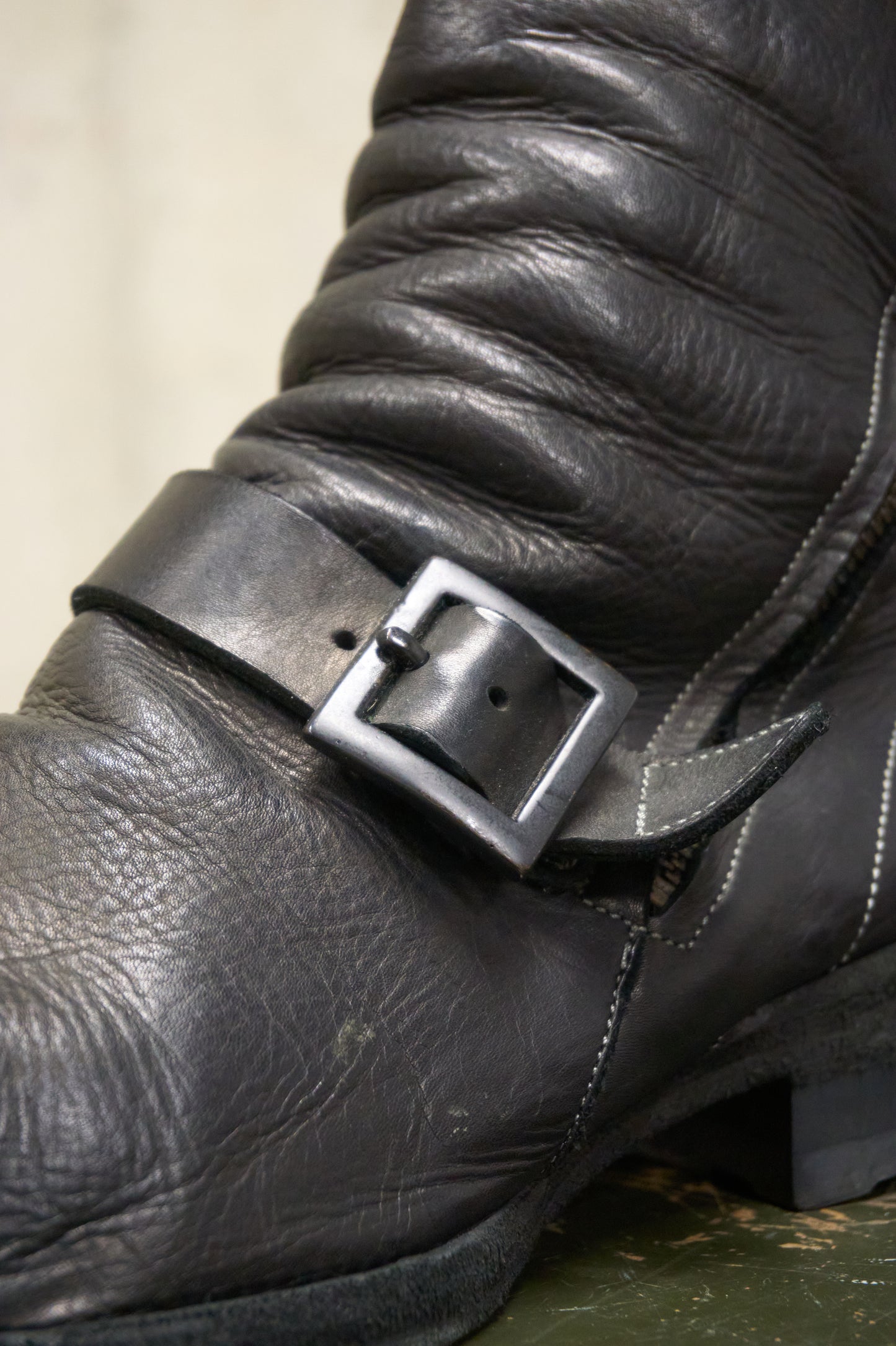 Close-up of a black leather boot with a buckle on a neutral background