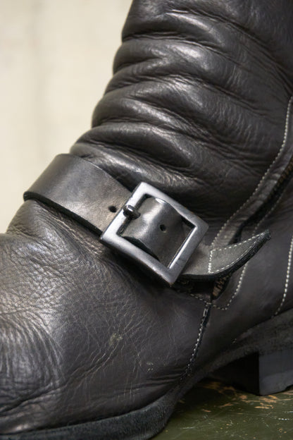 Close-up of a black leather boot with a buckle on a neutral background