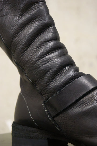 Close-up of a black leather boot with visible stitching on a neutral background