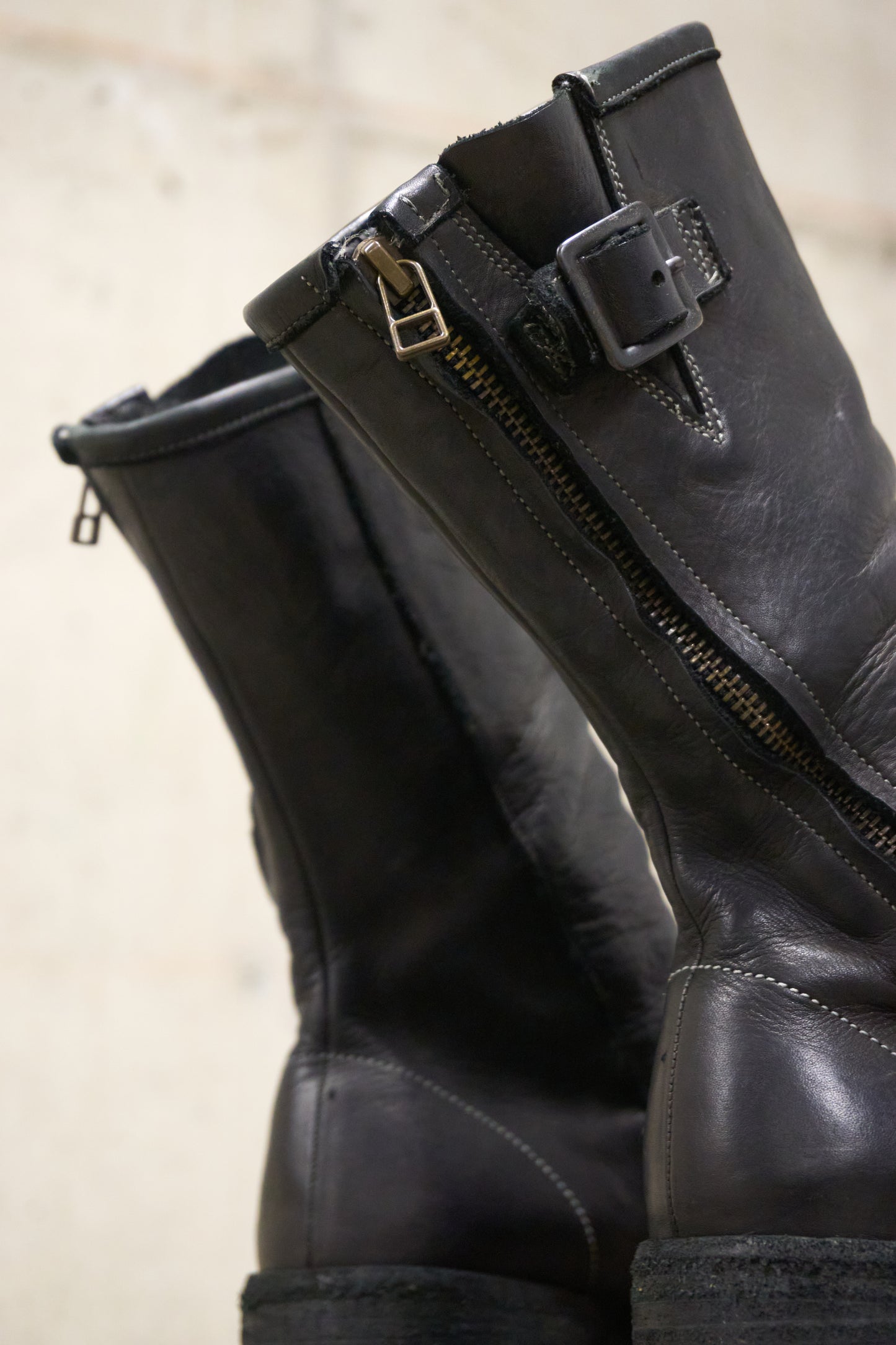 Pair of black leather boots with zippers on a beige background