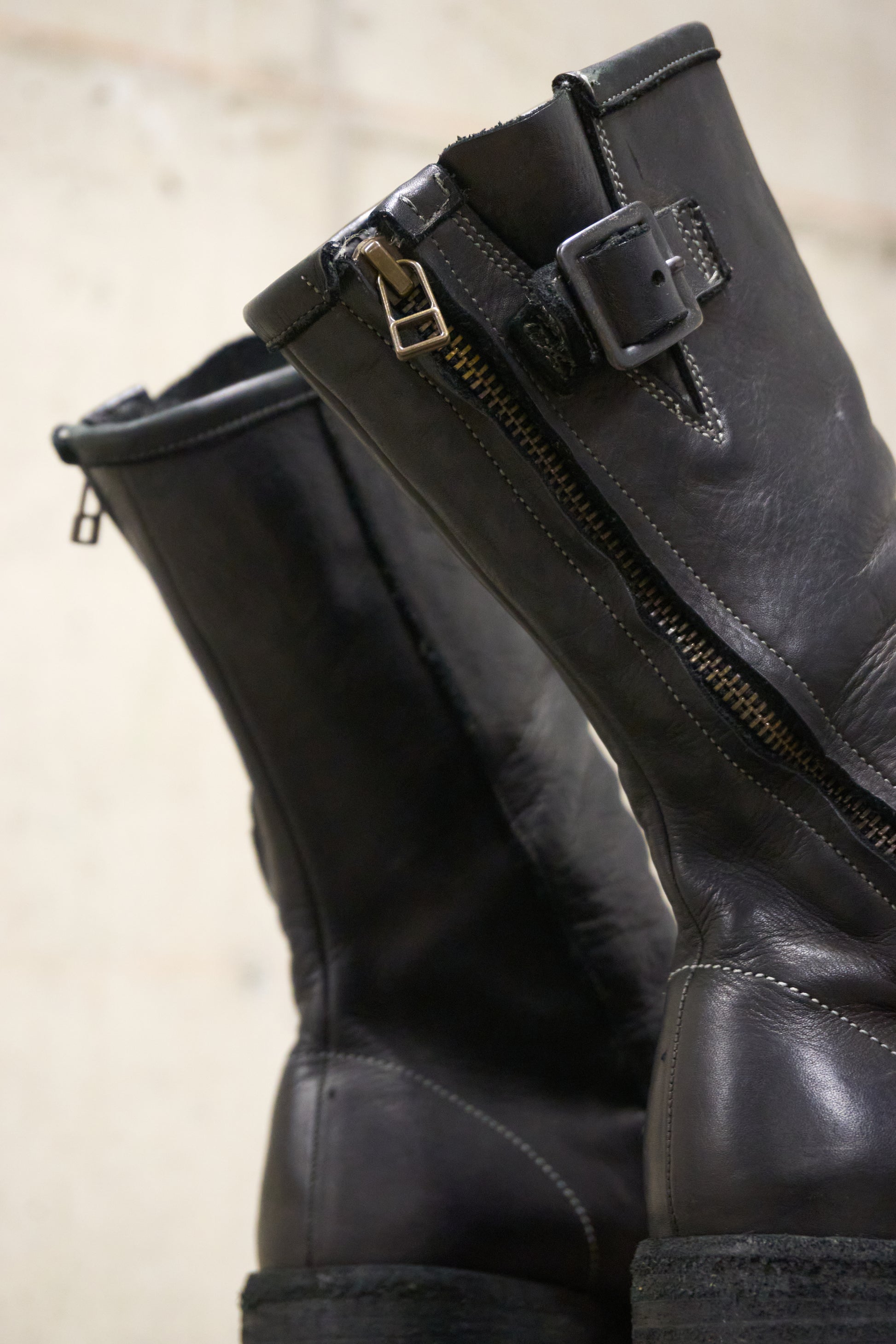 Pair of black leather boots with zippers on a beige background