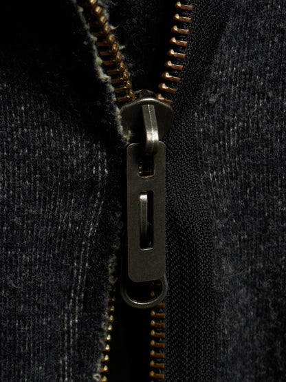 Close-up of a dark charcoal gray zippered garment with a dark metal zipper pull and gold-toned zipper teeth.