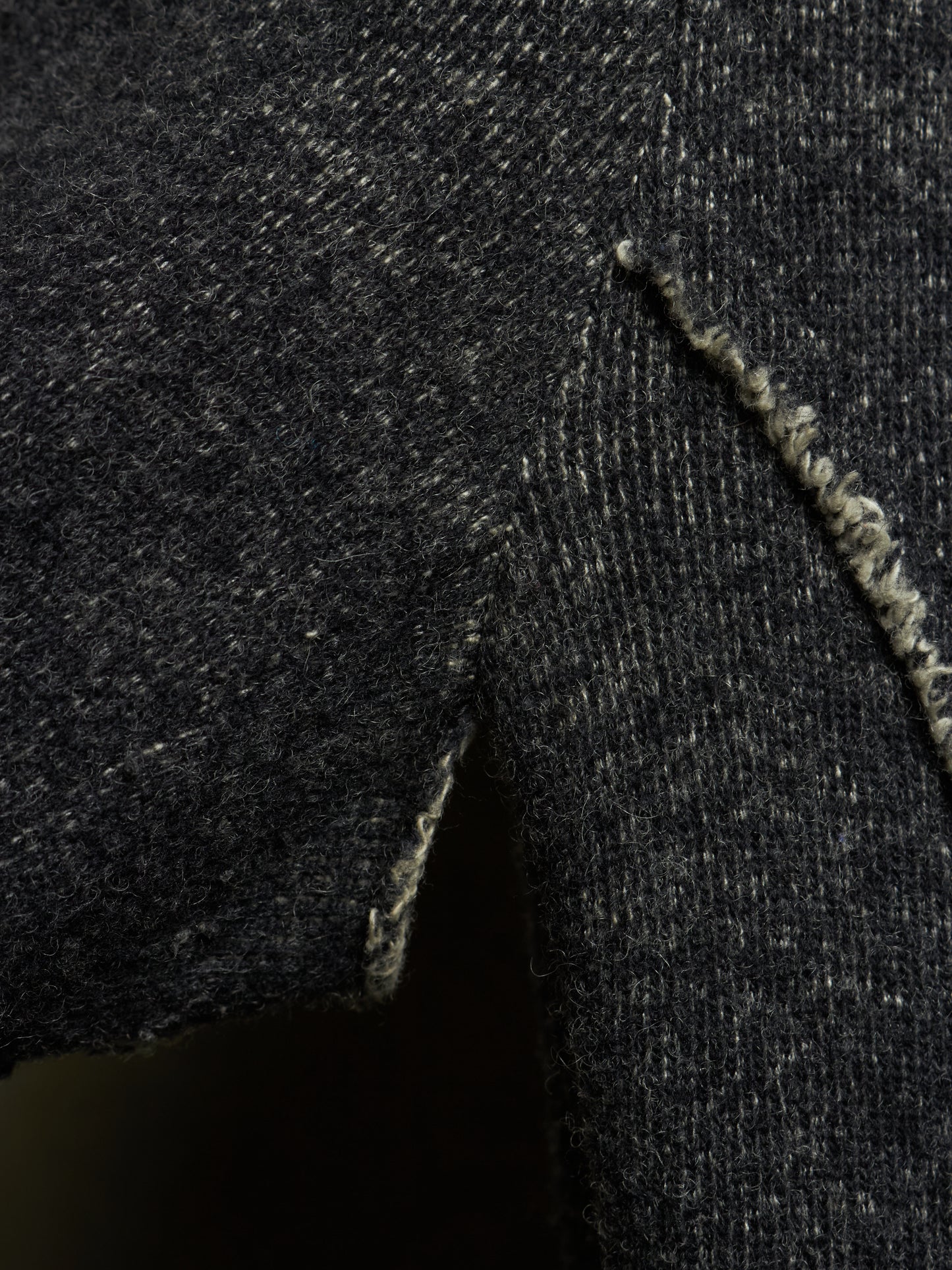 Close-up of a dark charcoal gray knit fabric with a visible frayed edge and textured weave.