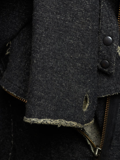 Close-up detail of a dark charcoal gray distressed denim jacket, showing the heavy textured fabric, raw frayed edges, metal snap buttons, and a brass zipper.