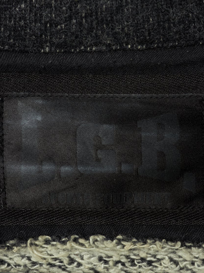 Close-up of a black woven fabric item with a dark translucent patch showing embossed letters and a textured cream and black fuzzy trim along the bottom edge.