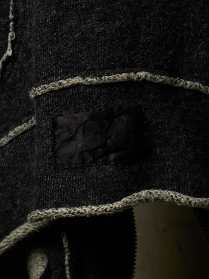 Close-up of a dark charcoal knit garment with contrasting light beige trim and a black patch detail.