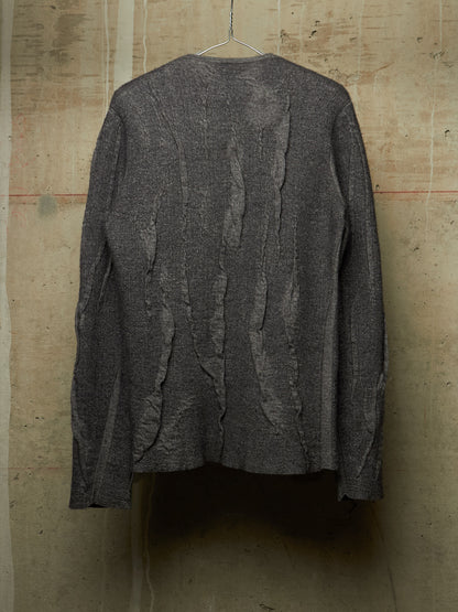 A dark gray textured knit cardigan sweater with vertical ruffled details, hanging on a wire hanger against a rustic concrete wall.