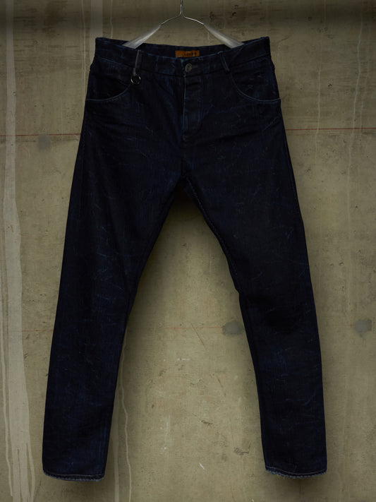Dark indigo denim jeans hanging on a metal hanger against a textured concrete wall.