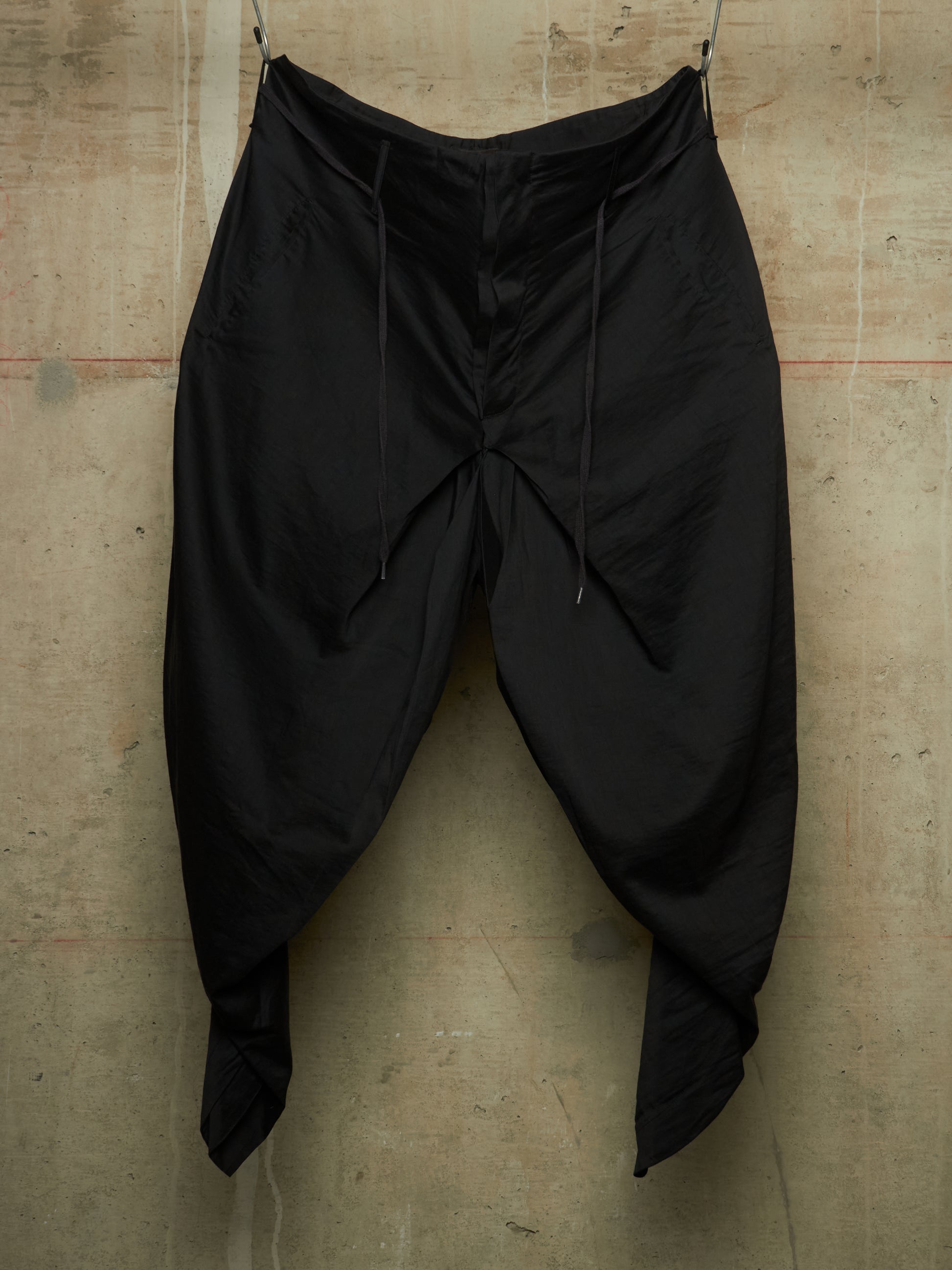 Black baggy drawstring pants hanging against a textured concrete wall.
