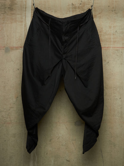 Black baggy drawstring pants hanging against a textured concrete wall.