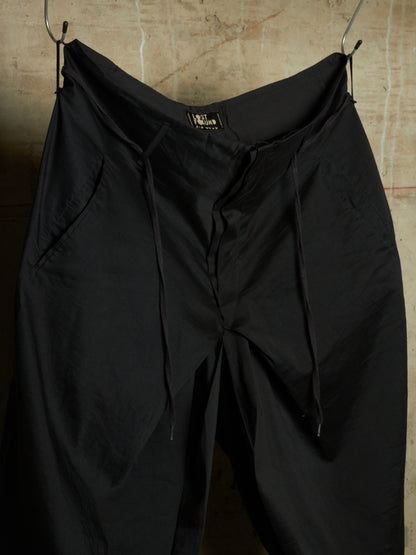 Black drawstring pants hanging from metal hooks against a textured concrete wall.