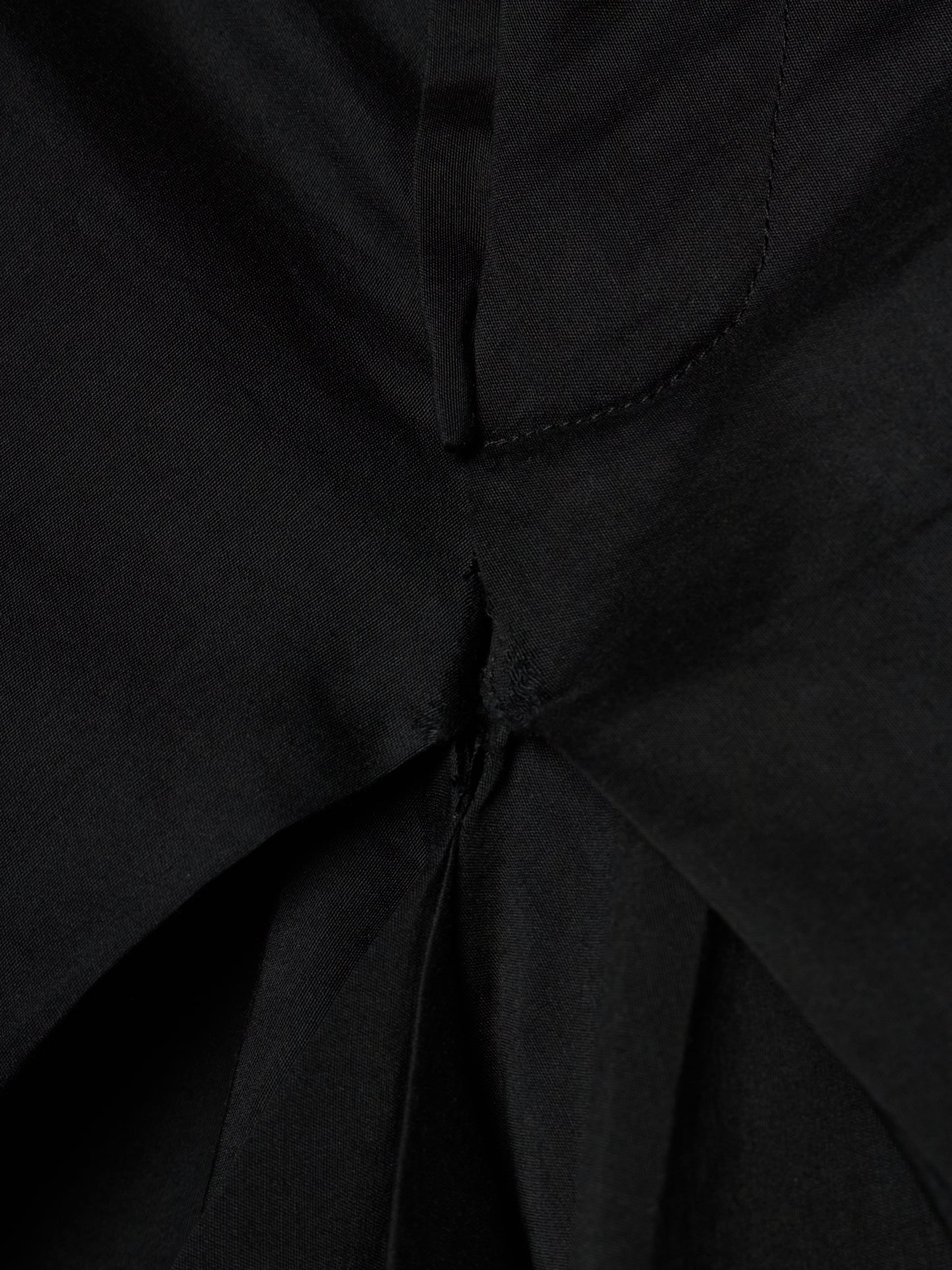 Close-up of a black fabric garment showing a gathered waist or pleated detail with visible stitching.