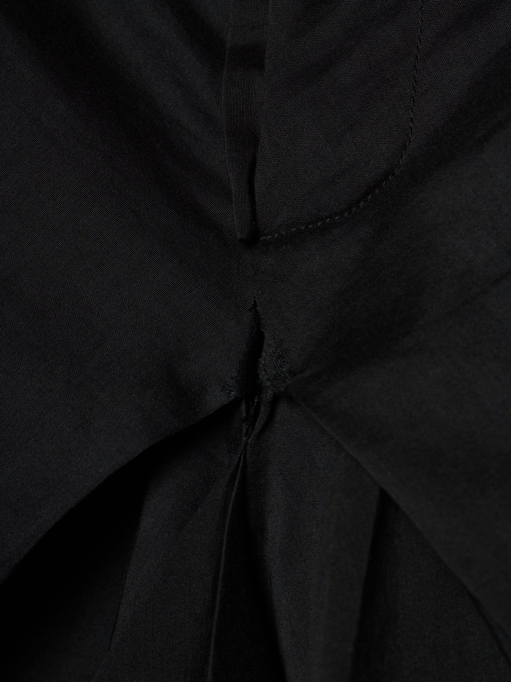 Close-up of a black fabric garment showing a gathered waist or pleated detail with visible stitching.