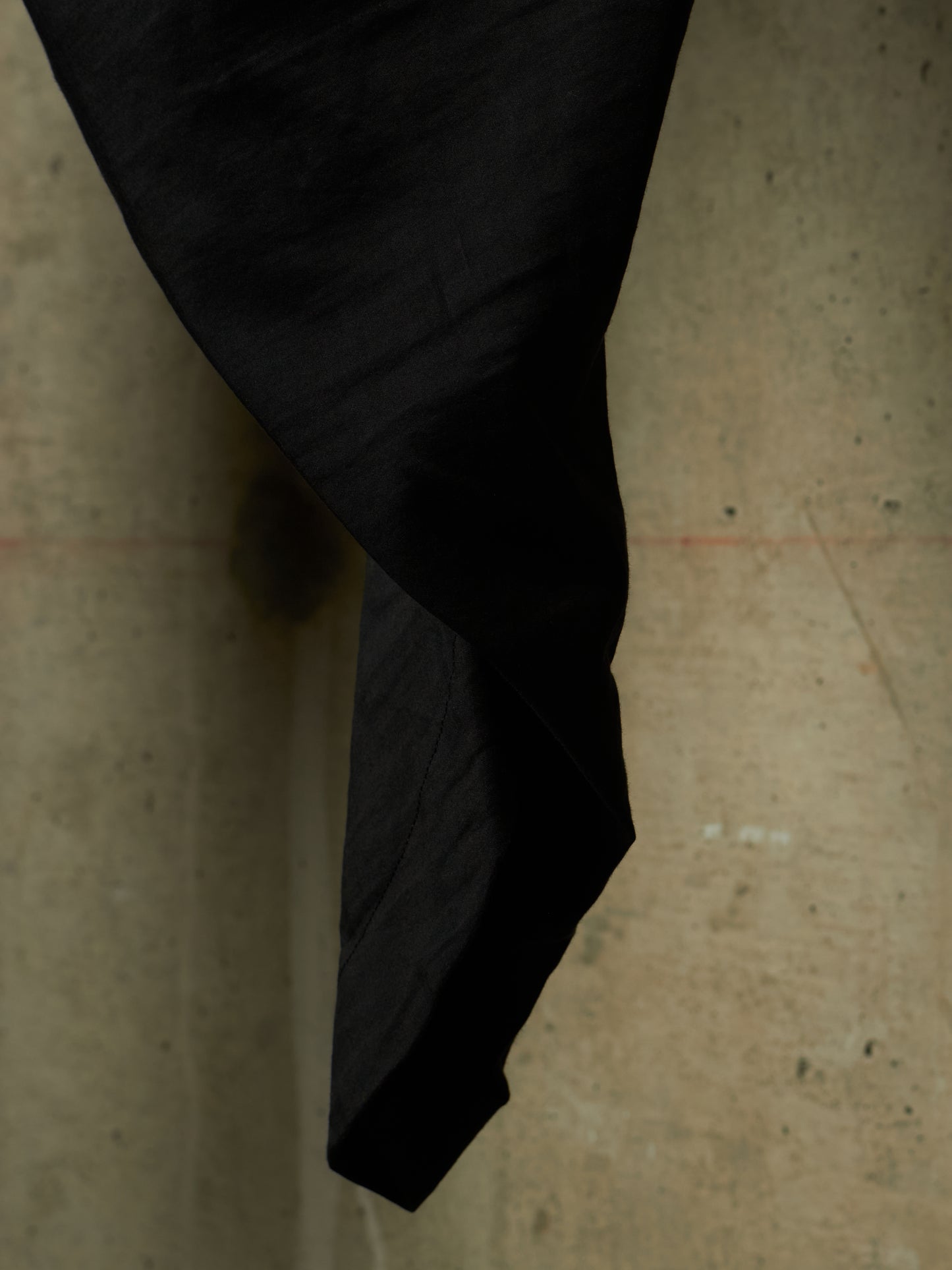 A close-up of a black fabric or garment draped and hanging against a textured concrete wall.