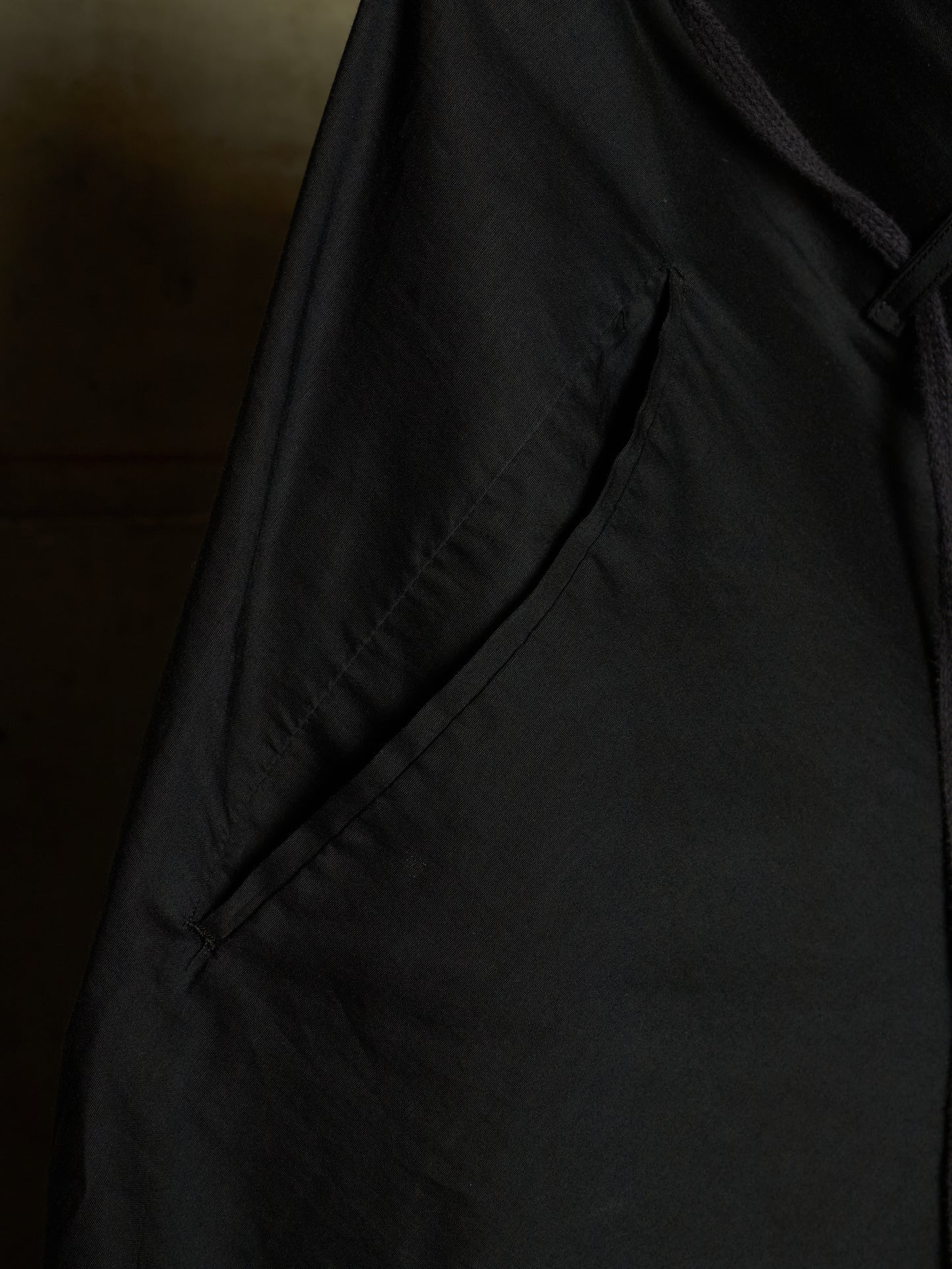 Close-up detail of a black garment, showing a side pocket with visible stitching and a dark drawstring or cord.