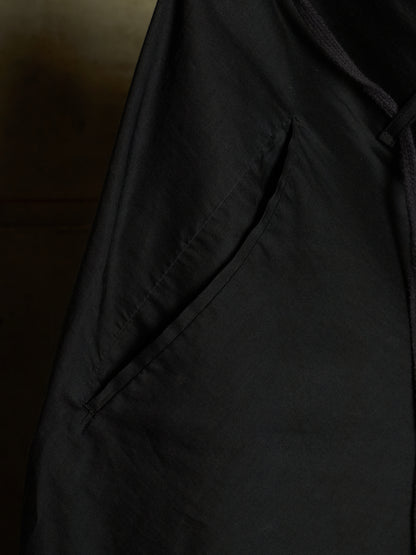 Close-up detail of a black garment, showing a side pocket with visible stitching and a dark drawstring or cord.