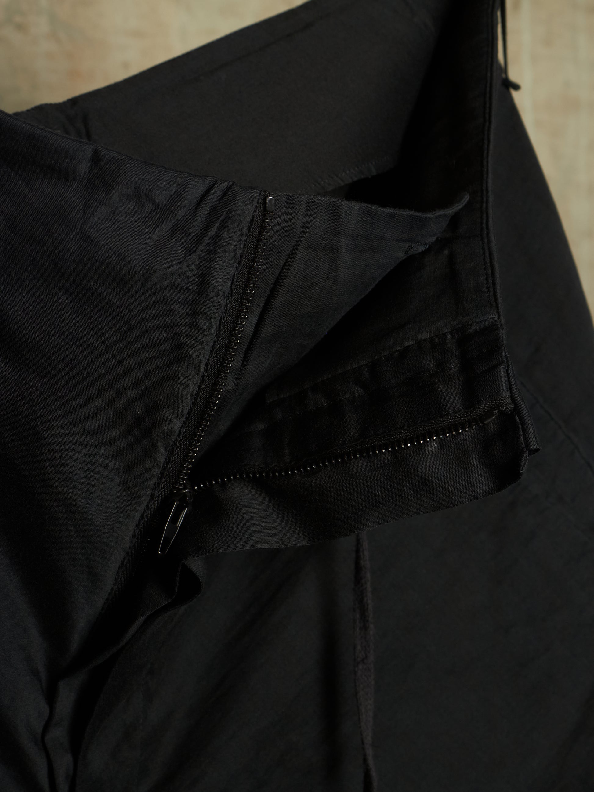 Close-up of a black lightweight jacket or windbreaker showing a zippered pocket and fabric texture.